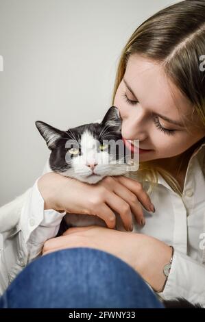 Schöne junge blonde Frau kuscheln ein gelangweilt jung schwarz und Weiße Katze aus der Nähe Stockfoto