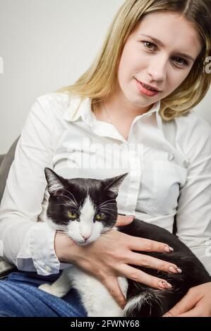 Schöne junge blonde Frau kuscheln ein gelangweilt jung schwarz und Weiße Katze aus der Nähe Stockfoto