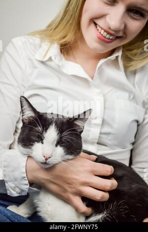 Schöne junge blonde Frau kuscheln ein gelangweilt jung schwarz und Weiße Katze aus der Nähe Stockfoto