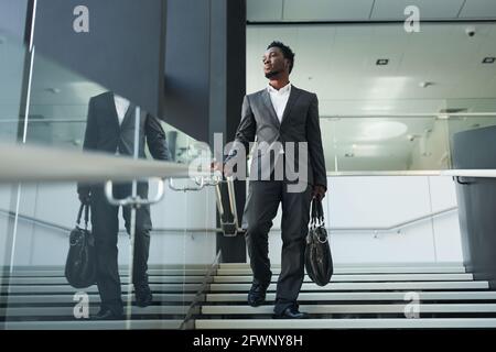 Porträt des erfolgreichen afroamerikanischen Geschäftsmannes, der im Bürogebäude die Treppe hinunter läuft und wegschaut, um Platz zu kopieren Stockfoto