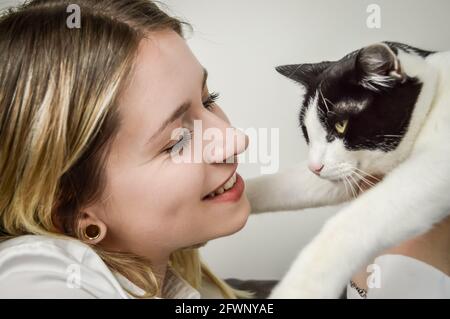 Junge und lächelnde blonde Frau mit einem jungen schwarzen und Weiß gefleckte Katze in der Nähe ihres Gesichts Stockfoto