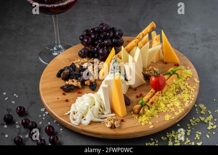Käseplatte mit Trauben, Marmelade, Feigen, Crackern und Walnüssen auf dunklem Steingrund Stockfoto