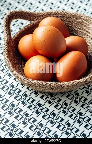 Frische goldene Eier in einem gewebten Naturkorb auf geometrischem Druck – FOODPIX WEISS, Platz für Text, TEXTRAUM Stockfoto