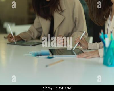 Eine kurze Aufnahme von zwei Designerinnen, die an einem digitalen Tablet arbeiten Und Verbrauchsmaterialien im Tagungsraum Stockfoto