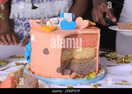 KAMPALA, UGANDA - 20. Apr 2021: Geburtstagskuchen in Scheiben geschnitten und Party-Kuchen mit schwarzen Leuten Händen im verschwommenen Hintergrund Stockfoto