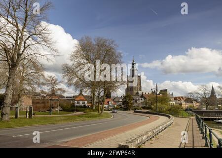 ZUTPHEN, NIEDERLANDE - 20. Apr 2021: Urbane, gewundene Asphaltstraße mit der holländischen hanseatischen mittelalterlichen Stadt Zutphen und dem Walburgiskerk-Turm im Hintergrund Stockfoto