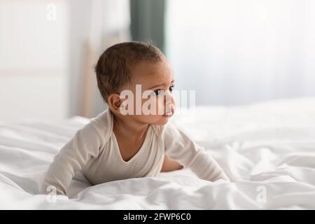 Niedliches kleines afroamerikanisches Baby, das zu Hause auf dem Bett kriecht Stockfoto