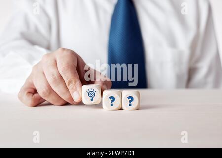 Um eine Lösung für Probleme oder kreative Ideen zu finden. Geschäftsmann Hand platziert Holzwürfel mit Idee Glühbirne Symbol neben Fragezeichen Symbole. Stockfoto