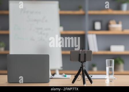 Arbeitsplatz des Tutors, des Lehrers während der covid Pandemie. Laptop, Notizblöcke, Smartphone auf Stativ, Wasser auf Tisch Stockfoto