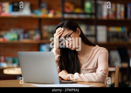 Enttäuschte arabische Dame mit Laptop und Probleme, arbeiten am Computer aus der Ferne im Café, leiden unter Kopfschmerzen Stockfoto