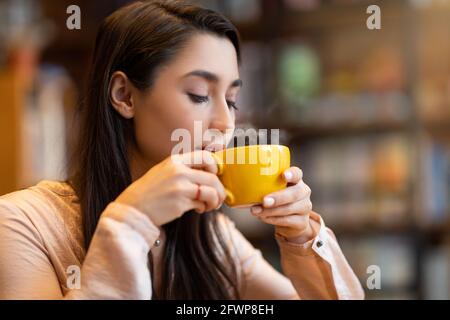 Entspannte arabische Frau riecht aromatischen Kaffee mit geschlossenen Augen und fühlt Harmonie, sitzt im Café, Kopie Raum Stockfoto