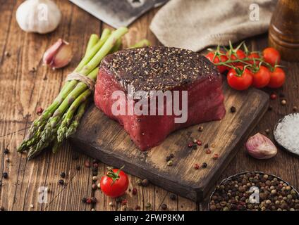 Ein Stück rohes Rindfleisch Oberschale mit Salz und Pfeffer auf Holz Schneidbrett mit Tomaten, Knoblauch und Spargelspitzen auf Holz Küche Tisch. Stockfoto