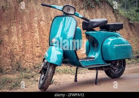 Vespa Scooter Vorderansicht, geparkt in einer schlammigen Straße an einem regnerischen Tag. Sky Blue Vintage Klassiker Motorrad. Stockfoto