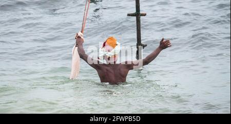 Der alte Stelzenfischer mit seiner Angelrute und leerer Tasche in den Händen schwimmt auf seine Bambusstange am Strand von Mirissa zu, fleißiger traditioneller Fisch Stockfoto