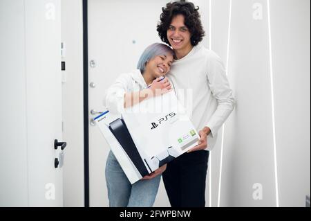 Ein glückliches junges Paar ist gerade mit einer brandneuen PlayStation 5-Spielekonsole von Sony aus dem Geschäft nach Hause gekommen. Sie haben es bei einem Black Friday-Verkauf bekommen. Moskau - November Stockfoto