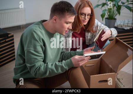 Neue Hausbesitzer haben an ihrer Wohnung angehalten, sie sortieren Kartons, ein Mann zeigt einer Frau sein altes Foto. Stockfoto