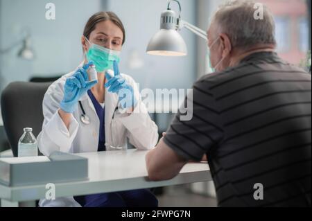 Eine junge Ärztin erklärt einem älteren Mann die Notwendigkeit, im Rahmen eines öffentlichen Impfprogramms gegen das Covid-19-Coronavirus geimpft zu werden. Stockfoto