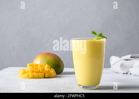 Gesunde Bio-Mango-Lassi, gefrorene Slushie oder Obst-Smoothies in Glas auf grauem Hintergrund. Indisches gesundes ayurvedisches kaltes Getränk mit Mango. Freshne Stockfoto