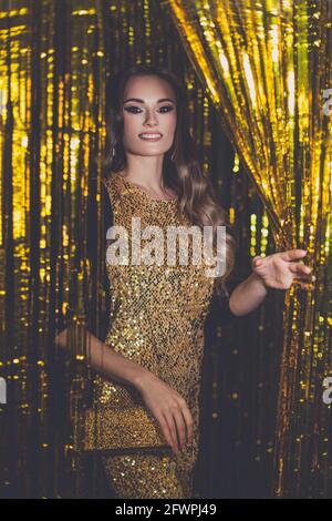 Glamouröse Frau Berühmtheit mit Make-up tragen Goldkleid lächelnd auf golden Bokeh Hintergrund Stockfoto