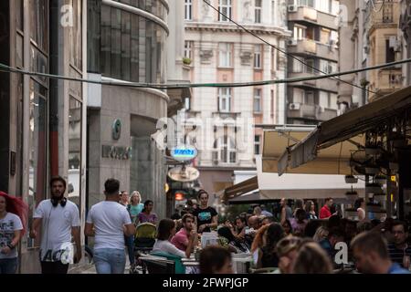 Bild einer vollgepackten Terrasse im Stadtzentrum von Belgrad, Serbien, Menschen sitzen in einem Café, während andere Menschen im Hintergrund feiern. Stockfoto