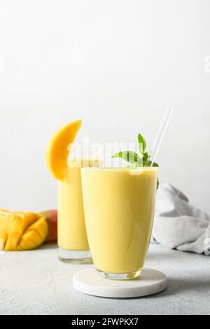 Zwei Mango-Lassi in Gläsern auf grauem Hintergrund. Indisches gesundes veganes Getränk mit Mango. Frische Lassi aus Joghurt, Wasser, Gewürzen, Früchten und Eis Stockfoto