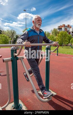 Ein älterer graubärtiger Mann übt im Freien auf öffentlichen Sportgeräten. Stockfoto