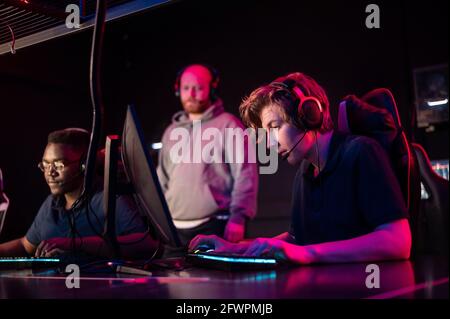 Während des Dota 2 Turniers spielen zwei Jungs aus dem Team an den Computern, der Trainer wacht von hinten. Stockfoto