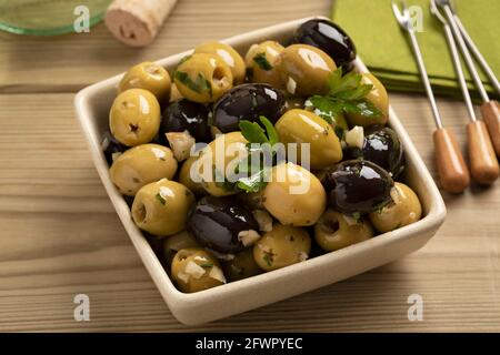 Schüssel mit grünen und schwarzen Oliven gewürzt mit Knoblauch und Kräuter aus der Nähe Stockfoto