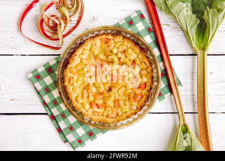 Oben Blick auf hausgemachten runden gebackenen Rhabarber ( Rheum hybridum ) Pie weiß rustikalen Holztisch Hintergrund. Rhabarberstiele an der Seite. Saisonales Dessert im Frühling. Stockfoto