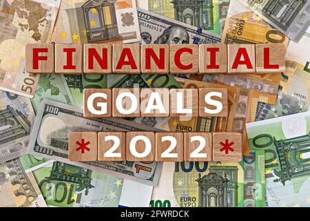 topview Foto zum Thema finanzielle Ziele. Holzwürfel mit der Aufschrift 'finanzielle Ziele 2022', auf dem Hintergrund von Dollar- und Euro-Scheinen. motiva Stockfoto