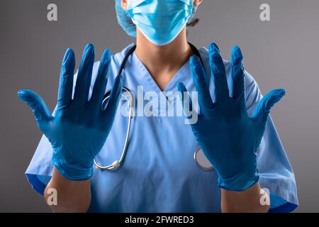 Mittlerer Abschnitt der weiblichen Chirurgen trägt OP-Handschuhe gegen grau Hintergrund Stockfoto