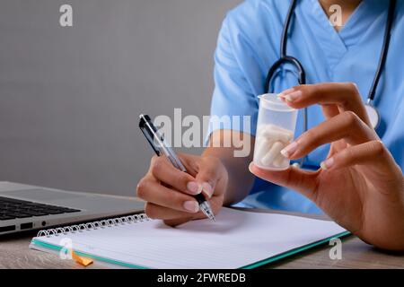 Mittlerer Abschnitt der weiblichen Gesundheitshelferin, die Medikamentenbehälter und hält Notizen machen Stockfoto