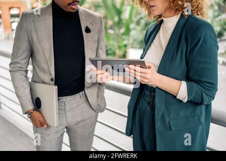 Unerkannte Geschäftsfrau, die formelle Kleidung trägt und mit ihrem Kollegen spricht und ein digitales Tablet benutzt. Stockfoto