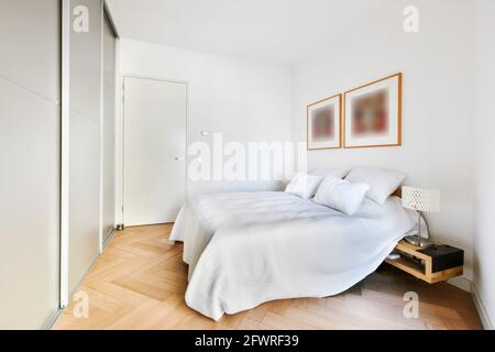 Komfortables Bett mit weißer Bettwäsche und Kissen im hellen Zimmer Mit Rahmen an der Wand und Einbauschrank Stockfoto