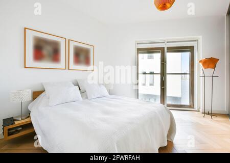 Komfortables Bett mit weißer Bettwäsche und Kissen im hellen Zimmer Mit Rahmen an der Wand und Einbauschrank Stockfoto