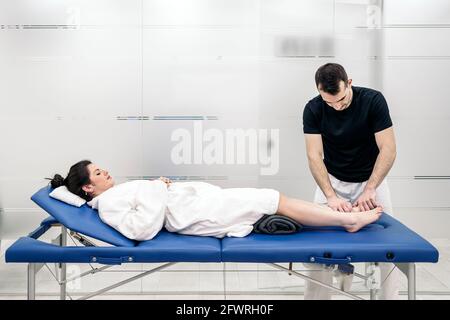 Männlicher Physiotherapeut, der entspannt auf einer Bahre liegende Frau eine Körpermassage gibt. Stockfoto