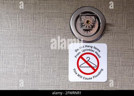 Hängen Sie keine Gegenstände auf den Sprinkler, da dies zu einem Überschwemmungsschild führen würde, das an einem Metallbrandsprinkler mit Wandhalterung in einem Hotelzimmer angebracht ist. Diese Elemente sind trig Stockfoto