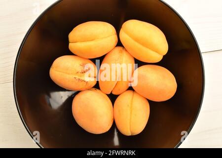 Mehrere organische gelbe Ananas-Aprikosen in einer Keramikplatte, Nahaufnahme, auf einem weißen Holztisch, Draufsicht. Stockfoto