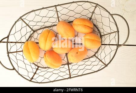 Mehrere organische gelbe Ananas-Aprikosen in einem Metallkorb, Nahaufnahme, auf einem weißen Holztisch, Draufsicht. Stockfoto