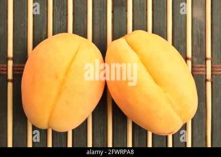 Zwei gelbe Ananas-Aprikosen auf einem Teller, Nahaufnahme, auf einer Bambusmatte, Draufsicht. Stockfoto