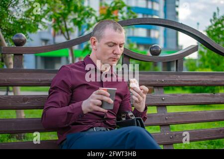 Traurige Büroangestellte isst einen süßen Donut mit Kaffee hinein Ein Stadtpark Stockfoto