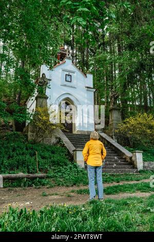Weibliche Reisende mit Blick auf kleine kleine Kapelle unserer Lieben Frau von Lourdes, Broumovsko Region, Tschechische republik.Rural katholische Kirche in Frühlingslandschaft. Stockfoto