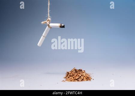 Welttag Der Tabakkontrolle. Auf blauem Hintergrund hängt eine ausgelöschte Zigarette über einem Stapel Tabak. Speicherplatz kopieren. Das Konzept der Nikotinsucht Stockfoto