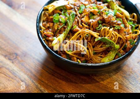 indische, chinesische, würzige Haka-Nudeln mit Hühnertofu-Paneer Gewürze und Kohl in eine schwarze Schüssel auf einem gelegt Wodden Tisch bereit, in einem zu essen Stockfoto