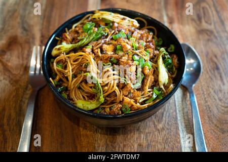indische, chinesische, würzige Haka-Nudeln mit Hühnertofu-Paneer Gewürze und Kohl in eine schwarze Schüssel auf einem gelegt Wodden Tisch bereit, in einem zu essen Stockfoto
