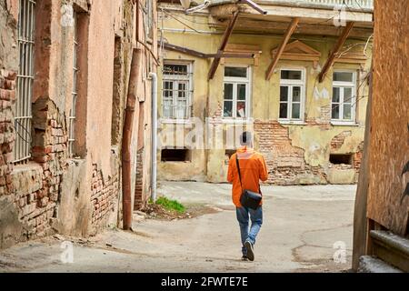 Ein einsamer Kerl geht in der Altstadt zwischen heruntergekommenen Häusern spazieren. Stockfoto