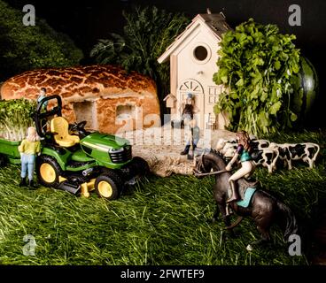 Miniaturfiguren auf einem Bauernhof. Ein Mädchen, das Pferd, ein Mann und eine Frau in der Nähe des Traktors, jemand, der die Kühe füttert, das Bauernhaus im Hintergrund. Stockfoto