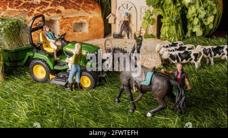 Miniaturfiguren auf einem Bauernhof. Ein Mädchen, das Pferd, ein Mann und eine Frau in der Nähe des Traktors, jemand, der die Kühe füttert, das Bauernhaus im Hintergrund. Stockfoto