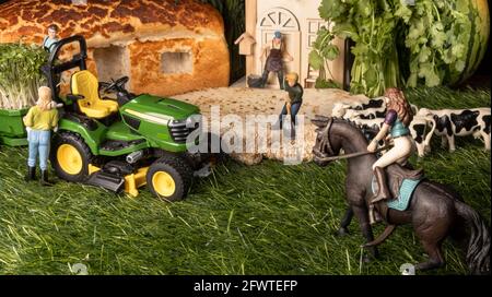 Miniaturfiguren auf einem Bauernhof. Ein Mädchen, das Pferd, ein Mann und eine Frau in der Nähe des Traktors, jemand, der die Kühe füttert, das Bauernhaus im Hintergrund. Stockfoto