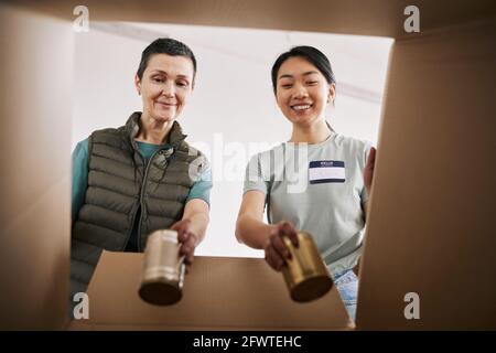 Portrait von zwei freiwilligen Helfern, die Lebensmittel aus der Dose in Schachteln legen Bei der Hilfe- und Spendenveranstaltung Stockfoto